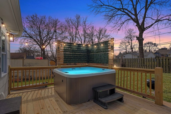 A hot tub on a wooden deck with a view of a house and trees.