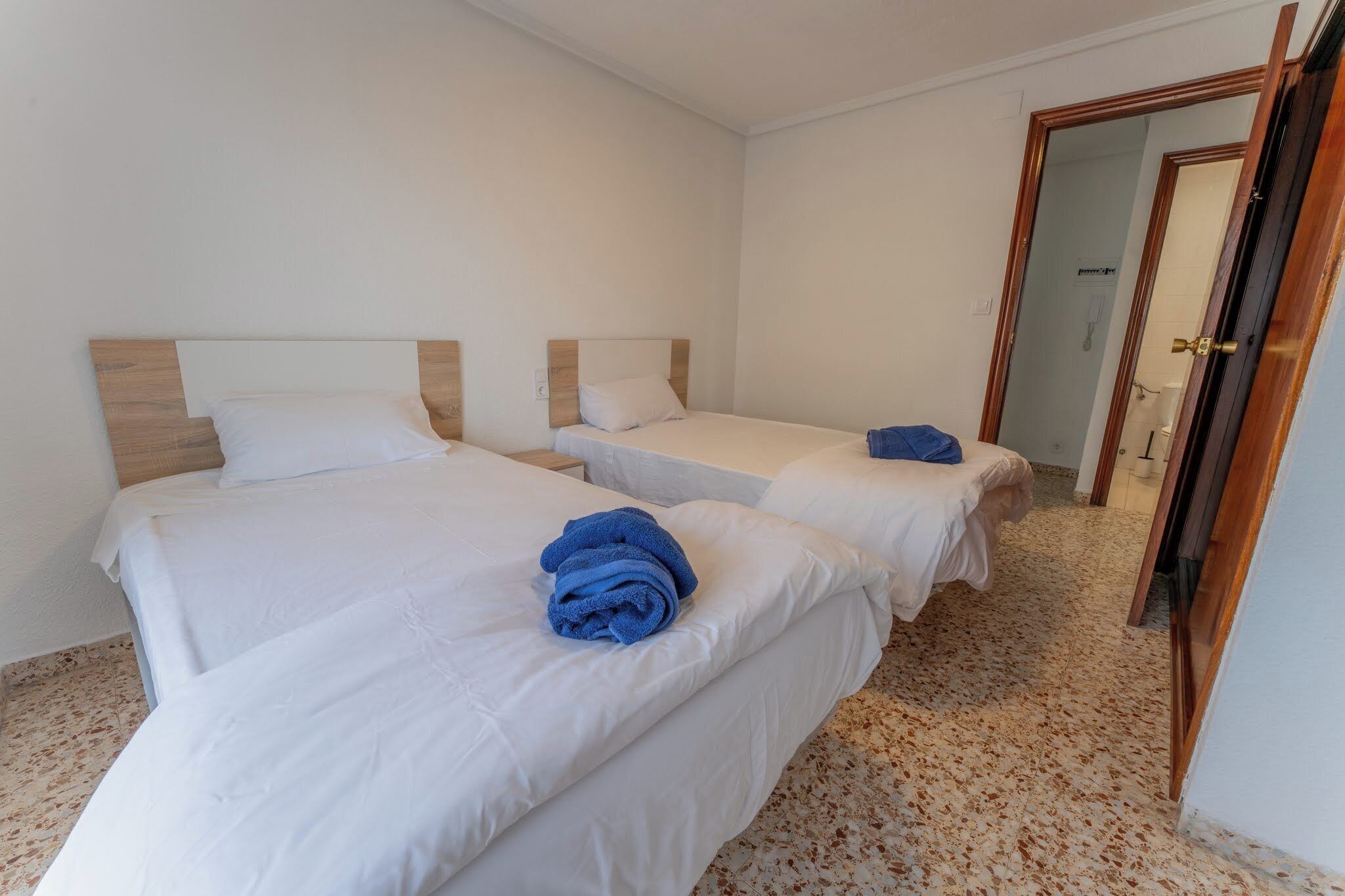 A hotel room with two single beds, a wooden headboard, white bedding, and a blue towel on one bed.