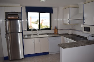 Una cocina con refrigerador de acero inoxidable, armarios blancos, lavavajillas, pileta y microondas.