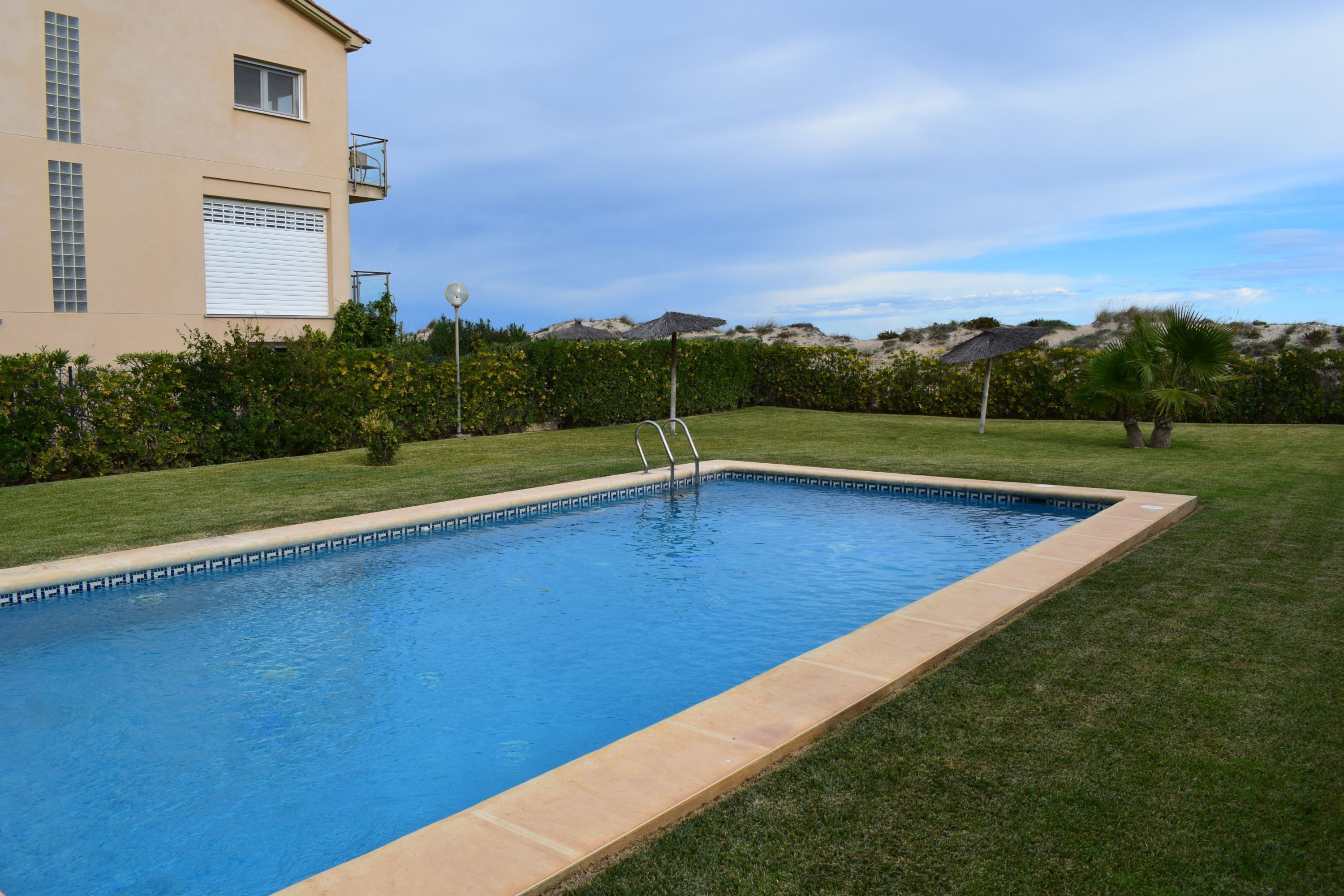 Ein rechteckiger Swimmingpool mit klarem, blauem Wasser, umgeben von einem gepflegten Rasen und einem Gebäude mit Balkon.