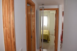 Un pasillo con puertas de madera y una cama con colcha estampada al fondo.