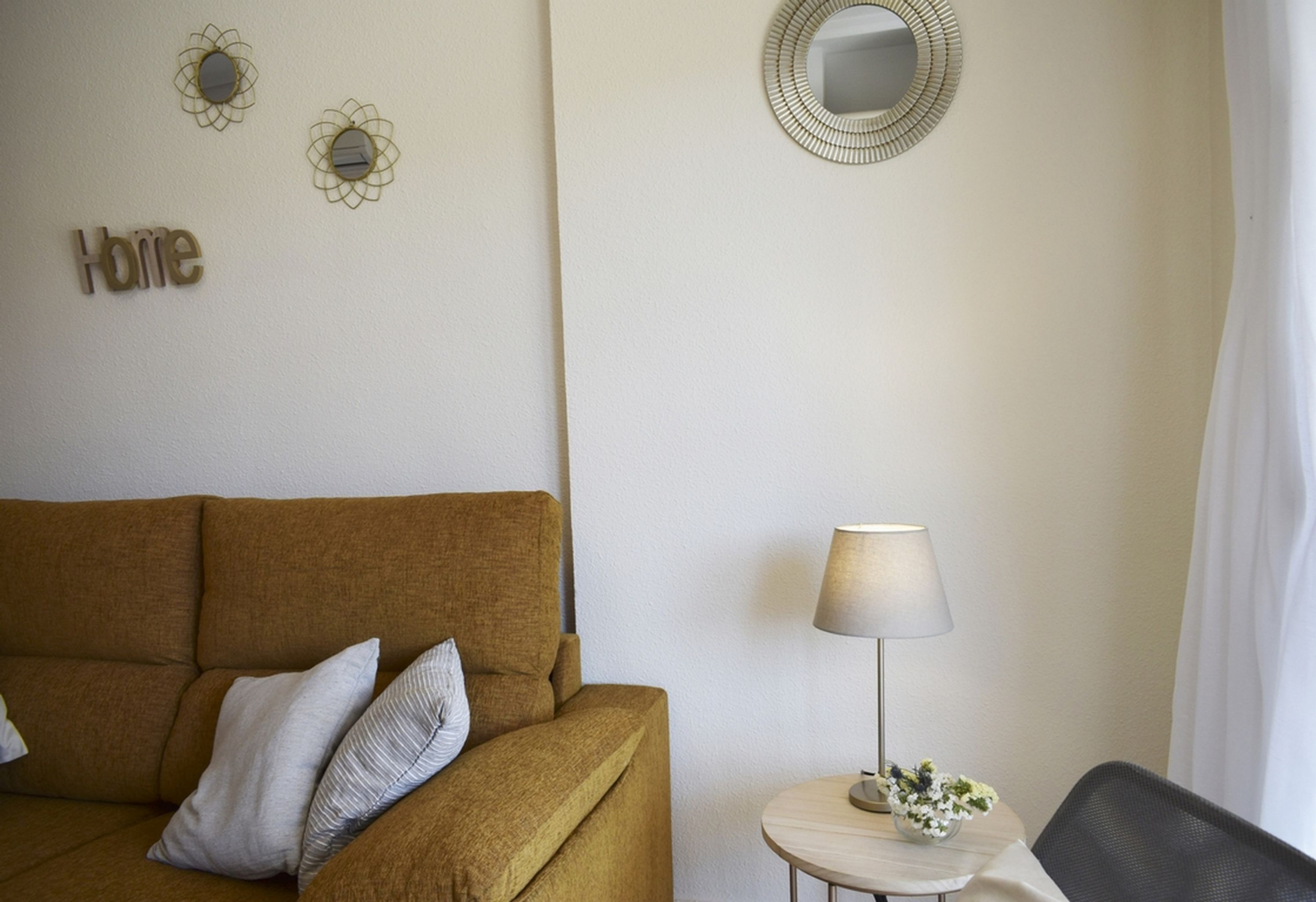 A room with a brown sofa, a small round table with a lamp, and a mirror on the wall.