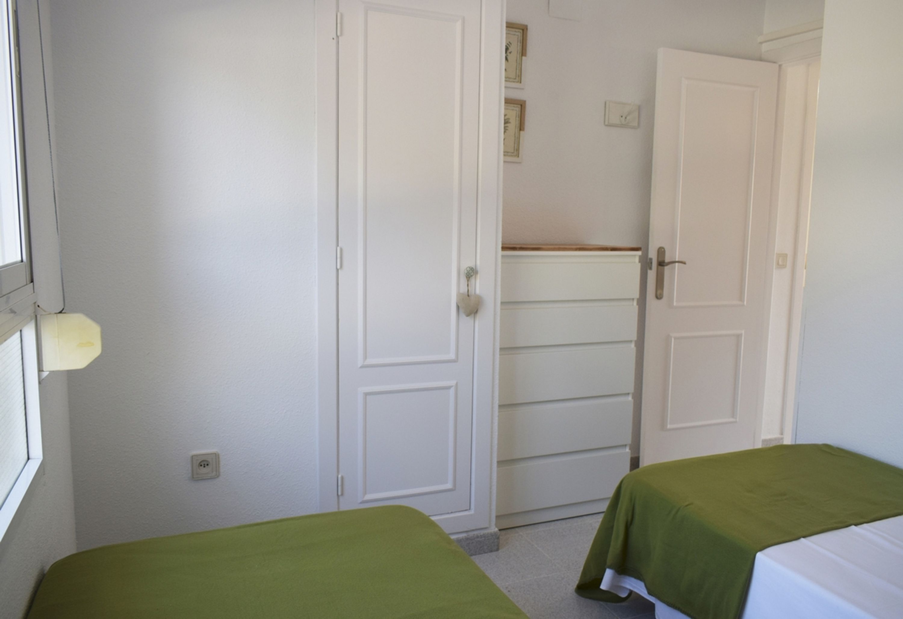 A bedroom with two beds, white walls, and a door leading to another room.