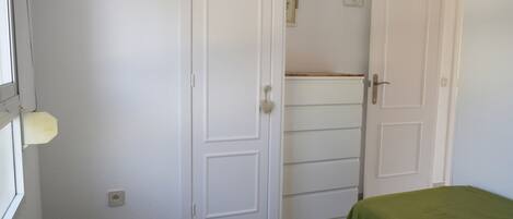A bedroom with two beds, white walls, and a door leading to another room.