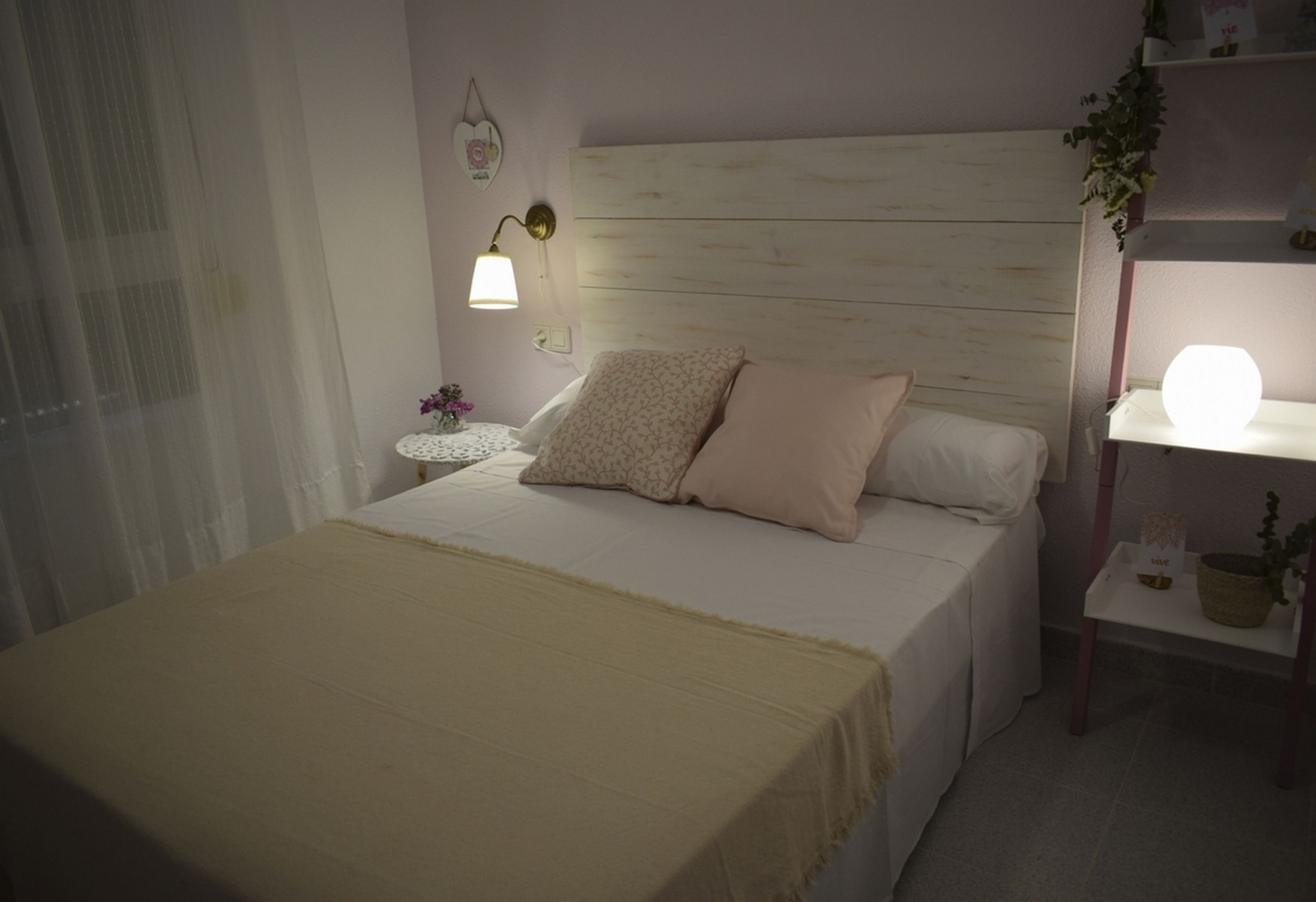 Et soveværelse med seng, natbord, lampe og en hylde med en plante.