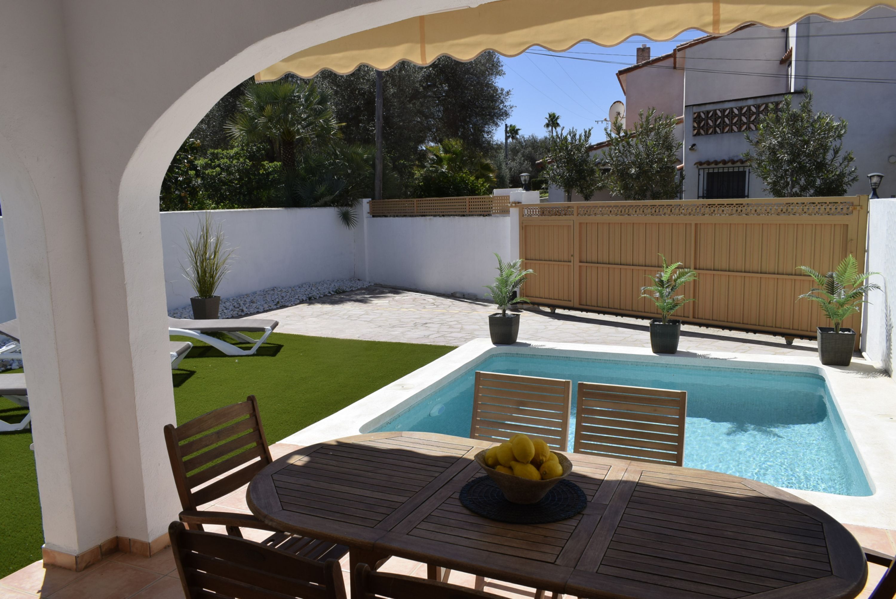 A poolside area with a table, chairs, and a bowl of fruit.