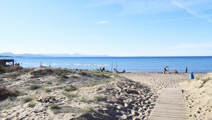 Una spiaggia sabbiosa con una passerella di legno che conduce all'acqua, ombrelloni e una postazione di salvataggio.