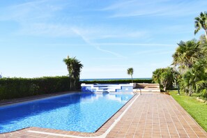 Una piscina con agua azul cristalina, rodeada por una terraza con baldosas y palmeras.