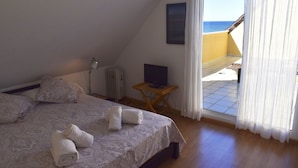 Una camera da letto con un letto, cuscini, una TV su un tavolino e vista mare da una porta finestra.