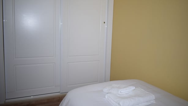 Ein Schlafzimmer mit einem Bett, weißen Handtüchern, einem Kleiderschrank und einer gelben Wand.