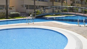 A swimming pool with a curved bridge, surrounded by a landscaped area with palm trees and a building in the background. - 02 Ap2106 in Denia With 2 Bedrooms and 1 Bathrooms (Denia)
