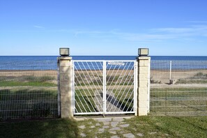 Portão fechado com vista clara do oceano e área cercada além.