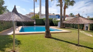A swimming pool with a thatched roof structure, surrounded by well-maintained grass and palm trees. - Ap2236 in Denia With 2 Bedrooms and 2 Bathrooms (Denia)