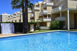 A swimming pool with a tiled border, surrounded by a residential building with balconies and a palm tree. - Ap2236 in Denia With 2 Bedrooms and 2 Bathrooms (Denia)