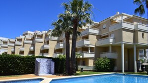 A swimming pool with a geometric tile pattern, surrounded by a landscaped area with palm trees and a building with multiple balconies. - Ap2236 in Denia With 2 Bedrooms and 2 Bathrooms (Denia)