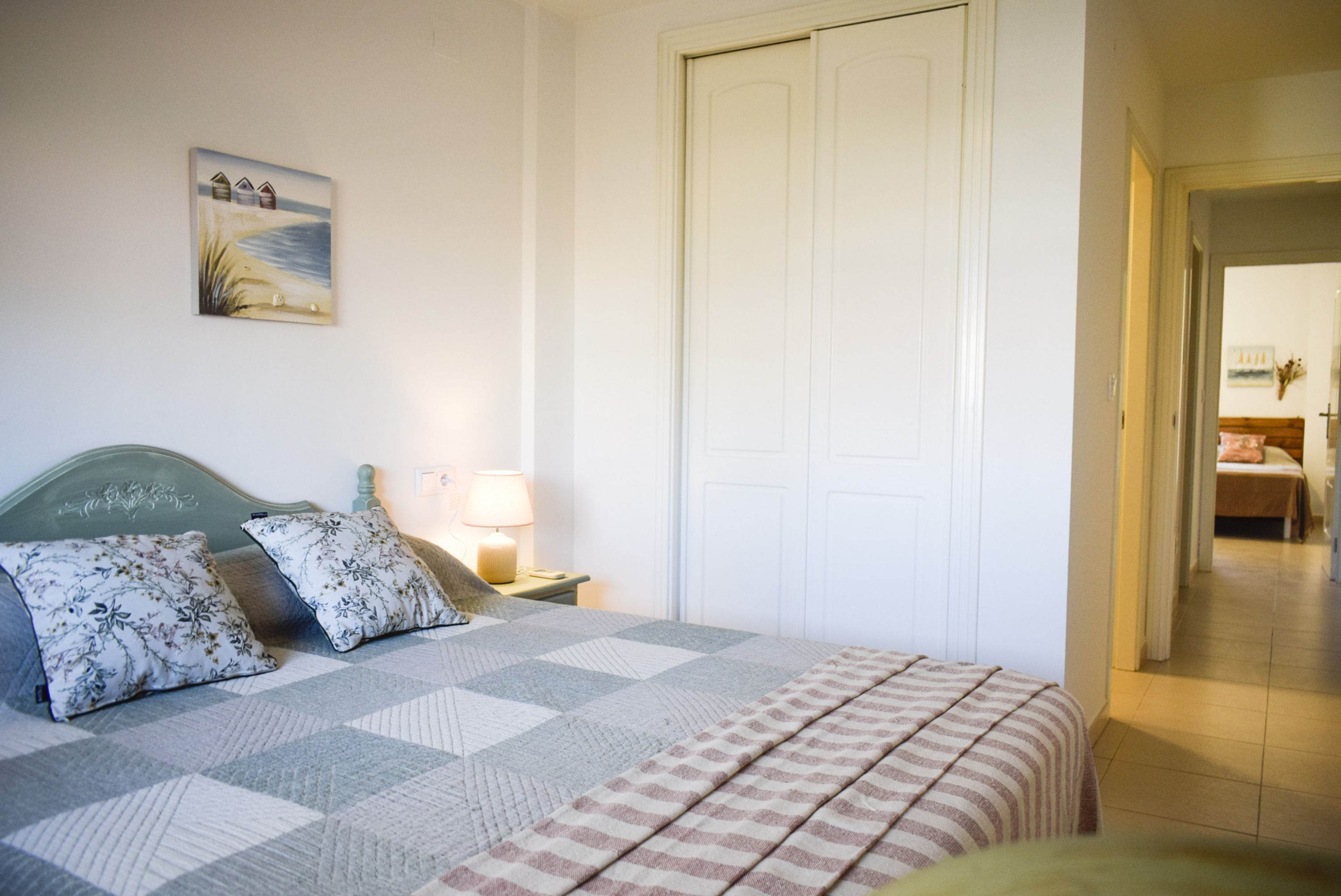 Quarto com cama, almofadas, mesa de cabeceira, luminária, quadro e porta.