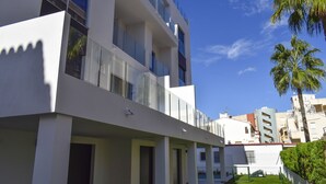 Ein modernes Mehrfamilienhaus mit Balkonen, einem gepflegten Rasen und Palmen.