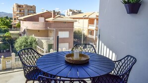 Ein Balkon mit rundem Tisch und Stühlen, einem Blumentopf und Blick auf angrenzende Gebäude.