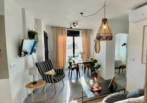 Uma sala de estar moderna com área de jantar, TV na parede e uma janela grande com cortinas.