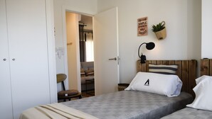 Ein Schlafzimmer mit Bett, Nachttisch, Lampe, einer Wandpflanze und einer Tür zu einem anderen Raum.