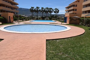 A swimming pool with a surrounding paved area, palm trees, and a mountain in the background. - At2214 in Denia With 2 Bedrooms and 2 Bathrooms (Denia)