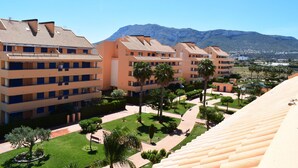 Un hotel de varios pisos con balcones, un patio con palmeras y montañas al fondo.