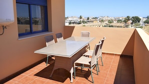 Un balcón con una mesa de vidrio y sillas de mimbre, con vistas a un pueblo costero.