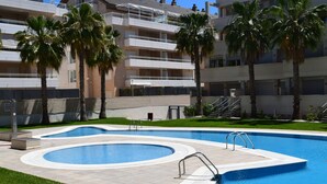 Ein Pool mit geschwungener Form, umgeben von Palmen und einem mehrstöckigen Gebäude mit Balkonen.