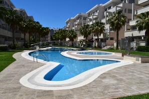 A swimming pool with a curved design, surrounded by a tiled deck and palm trees. - Ap2107 in Denia With 2 Bedrooms and 1 Bathrooms (Denia)