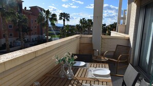 Ein Balkon mit Holztisch, gedeckt für zwei Personen, mit weißen Tellern, Besteck und zwei Glasvasen mit Blumen.