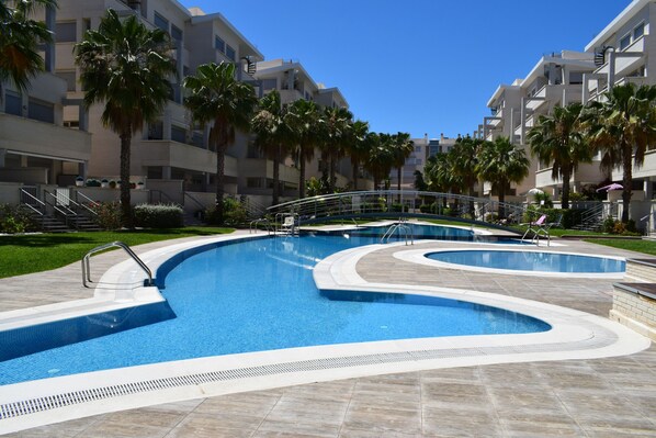 A swimming pool with a wavy design, surrounded by palm trees and modern buildings. - Ap2107 in Denia With 2 Bedrooms and 1 Bathrooms (Denia)