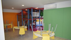 Ein Spielbereich für Kinder mit Netzumrandung, gelben Stühlen und einer Spielkonstruktion.