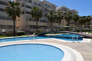 A swimming pool area with multiple pools, palm trees, and a modern apartment building in the background. - Ap2107 in Denia With 2 Bedrooms and 1 Bathrooms (Denia)