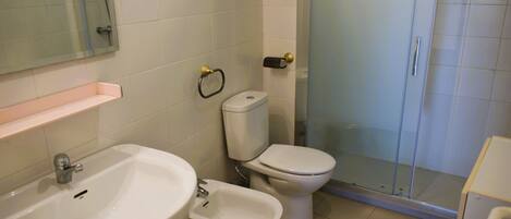 A bathroom with a sink, bidet, toilet, and a glass shower enclosure.