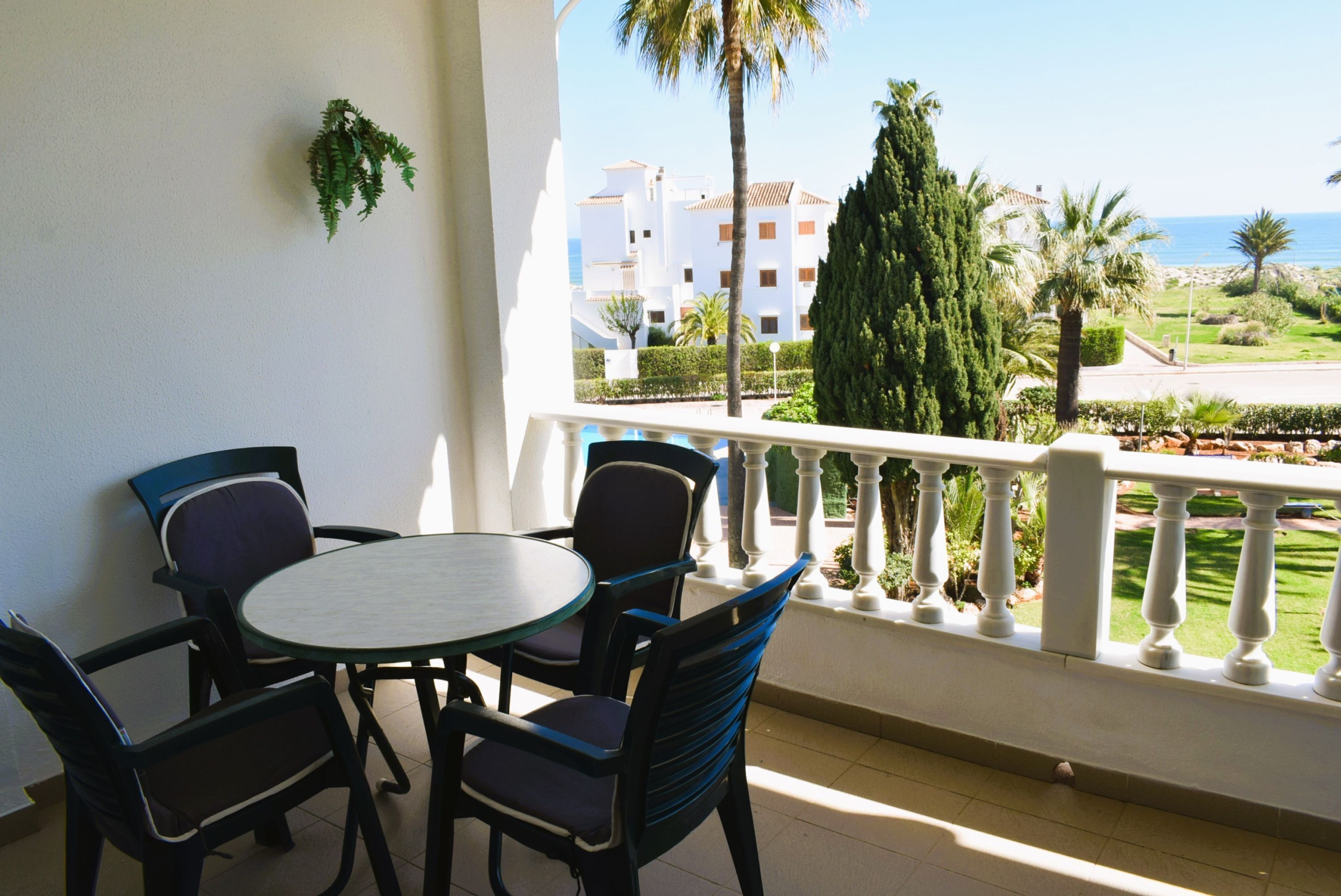 Un balcon avec une table et des chaises, donnant sur une zone côtière avec des bâtiments et des palmiers.