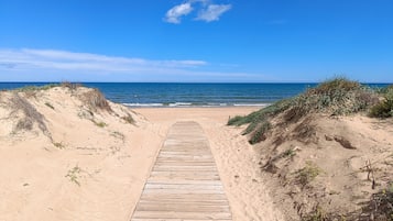 A wooden boardwalk leading to a beach with clear skies and calm sea.