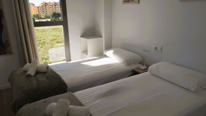 A hotel room with two beds, a window with a view of buildings, and a bedside table with a lamp. - Ap2242 in Denia With 2 Bedrooms and 2 Bathrooms (Denia)