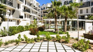 A modern residential building with multiple balconies, a central courtyard with palm trees, and a paved walkway. - Ap2242 in Denia With 2 Bedrooms and 2 Bathrooms (Denia)