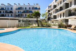 A swimming pool surrounded by modern apartment buildings with balconies, a covered seating area, and a small garden. - Ap2242 in Denia With 2 Bedrooms and 2 Bathrooms (Denia)