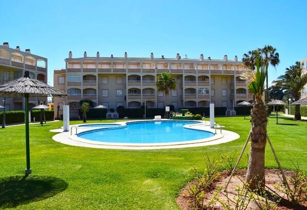 Una piscina rodeada por un césped bien cuidado, con un edificio de varios pisos al fondo.
