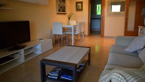 A modern living room with a flat-screen TV, a coffee table with books, a grey sofa, and a dining area with chairs and a table. - Ap2215 in Denia With 2 Bedrooms and 2 Bathrooms (Denia)