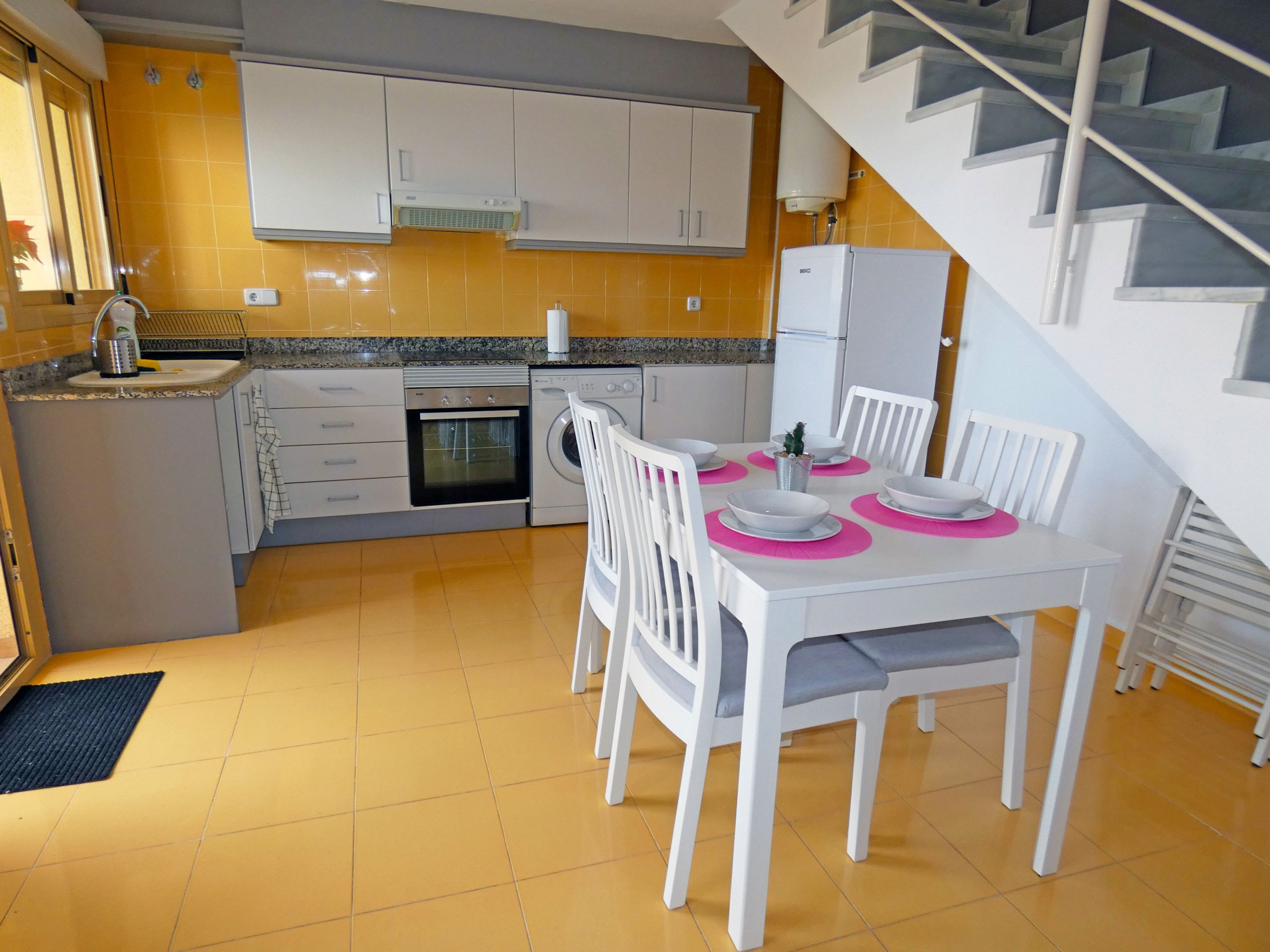 A compact kitchen with a dining area, featuring a built-in oven, a washing machine, and a refrigerator.