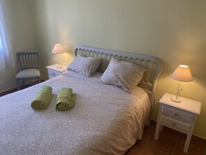 A neatly made bed with patterned bedding, two pillows, and two rolled towels. There are two bedside tables with lamps, a chair, and a wall-mounted light fixture. - Ch401 in Oliva With 4 Bedrooms and 2 Bathrooms (Oliva)