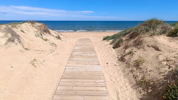 Une promenade en bois qui mène à une plage, avec un ciel dégagé et une mer calme.