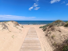 A wooden boardwalk leading to a beach with clear skies and calm sea.