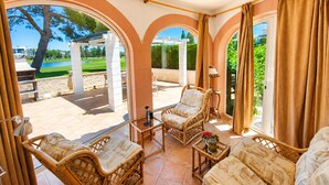 Une vaste terrasse dotée de meubles en osier, offrant une vue sur un terrain de golf et agrémentée d’une pergola.