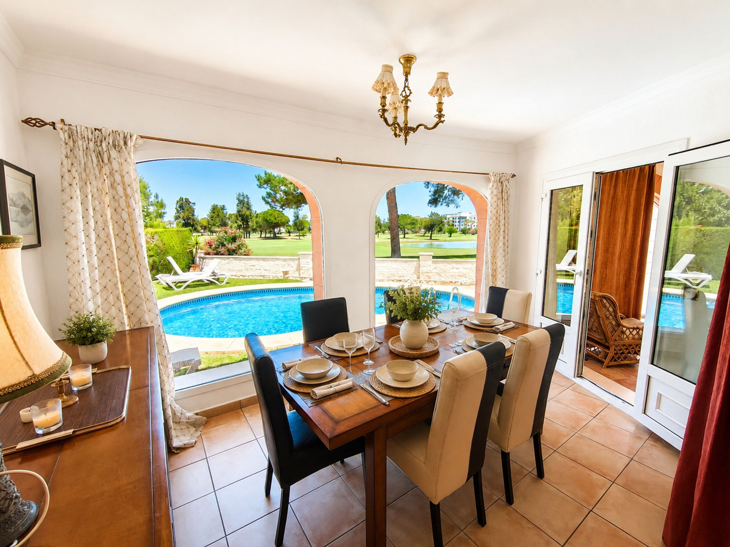 A dining area with a view of a swimming pool and garden.