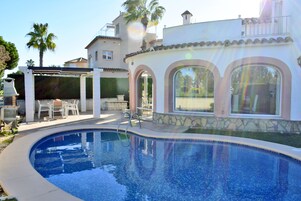 A swimming pool with a patio area, a pergola, and a stone wall.