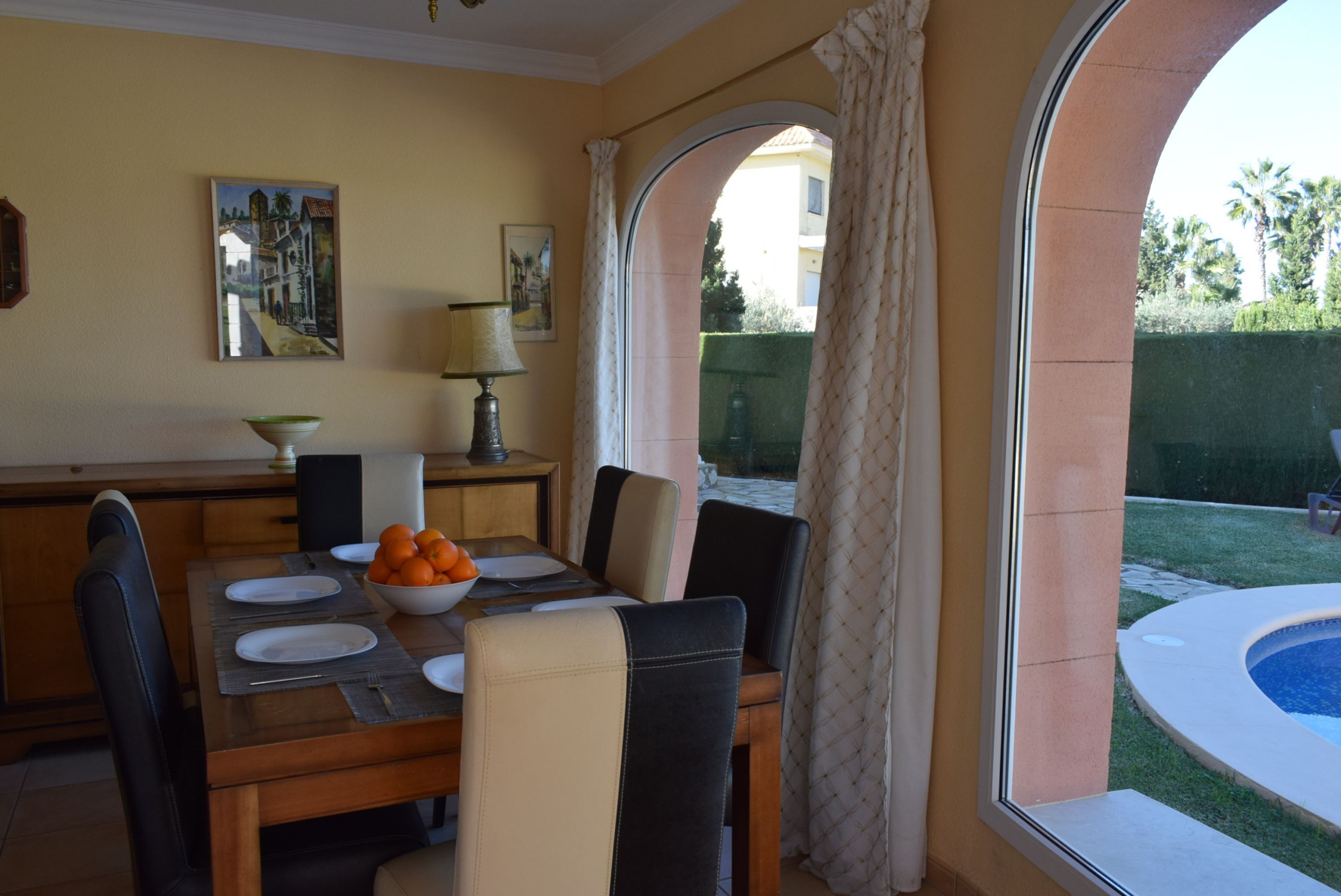Un comedor con una mesa dispuesta para cuatro personas, un cuenco de fruta y una lámpara sobre la mesa.
