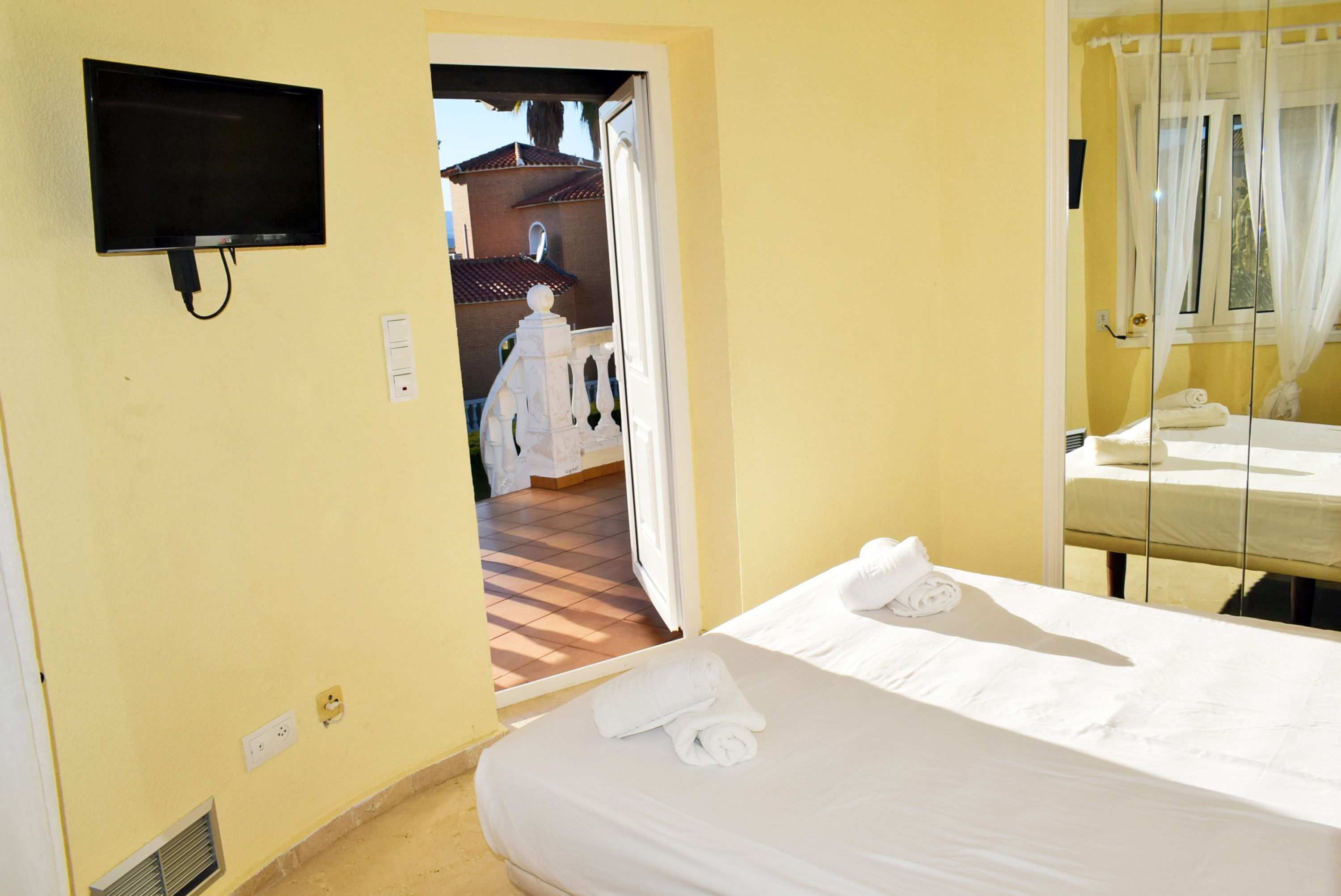 Habitación de hotel con cama, televisor montado en la pared y ventana con cortinas.